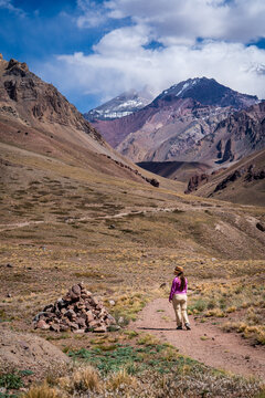 Mujer senderista recorrindo los senderos del Parque Provincial Aconcagua, pasando al lado de una t&iacute;pica selallizaci&oacute;n local de rocas, llamada apacheta.