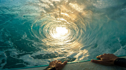 A surfer's view from inside a turquoise ocean wave barrel with sunlight shining through the water.