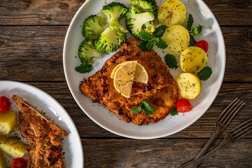 Crispy air fryer breaded pork chop with broccoli and boiled potatoes on wooden table. Top view	