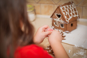 A child carefully decorates a gingerbread house, adding sweet details with frosting and candy