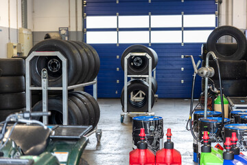 Racing tires stored racks inside motorsport garage service equipment fluids prepared competition. Professional paddock environment preparation precision performance endurance racing technology