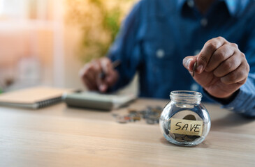A man hand putting coins into glass bottle saving bank for account save money. Planning step up, saving money for future plan, retirement fund. A business investment-finance accounting concept.