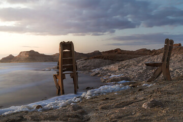 A chair on the edge of the rocky island in front of the lake at sunset