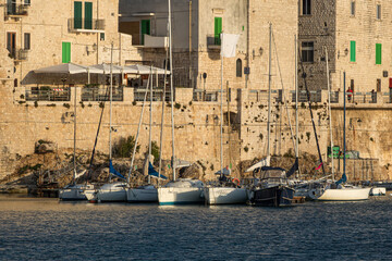 Sailboats docked by historic stone buildings at golden hour