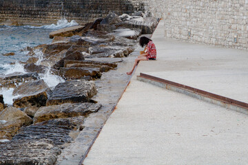 Lonely girl sitting near seawall and crashing waves