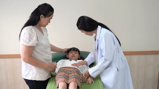 Asian female doctor pediatrician pressing stomach of sick girl patient lying on bed to check abdominal pain. Mother standing nearby in hospital ward. Stomachache, food poisoning, medical exam concept.
