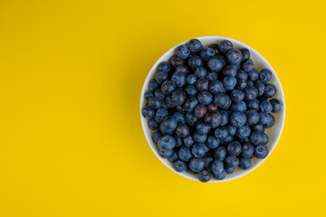 Fresh blueberries in a white bowl on a bright yellow background ready for eating or cooking