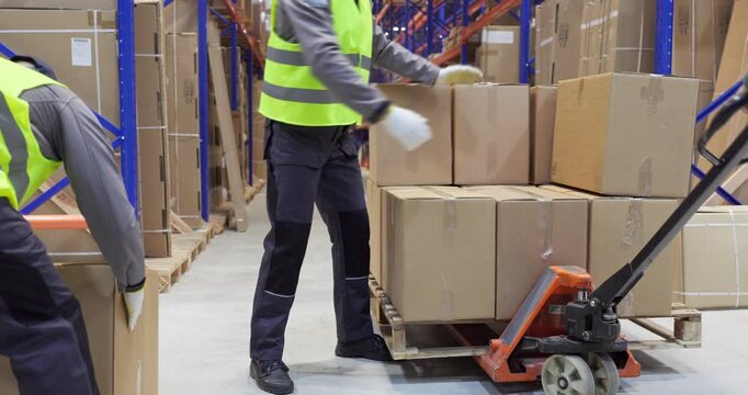 Warehouse workers loading pallet boxes for shipping. Manual pallet jack moves cartons in a distribution warehouse for efficient transport and safe loading. Strong concept of delivery logistics.