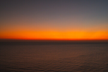 Minimalist ocean sunset with a smooth orange and blue sky gradient above calm sea water, creating a peaceful abstract seascape ideal for background, meditation, nature, and atmospheric design concepts