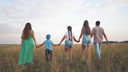 Rear view of family walking through field. Family walking in field holding hands. A woman and a man in nature in summer. A family is seen from behind as they walk through a field lifestyle.