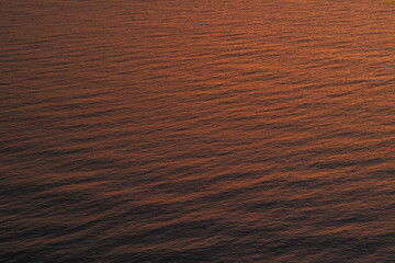 Abstract ocean water surface reflecting warm sunset light with gentle ripples, creating a calm and minimal natural texture suitable for background, luxury design, mindfulness, and atmospheric concepts