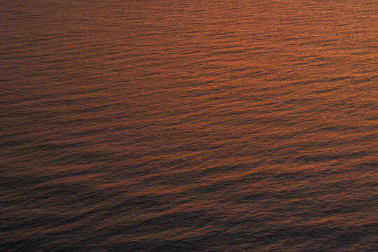 Abstract ocean water surface reflecting warm sunset light with gentle ripples, creating a calm and minimal natural texture suitable for background, luxury design, mindfulness, and atmospheric concepts