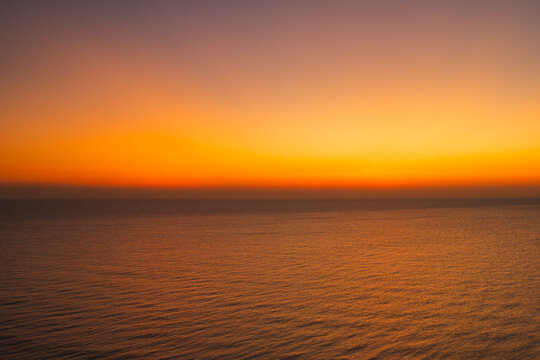 Minimalist ocean sunset with a smooth orange and blue sky gradient above calm sea water, creating a peaceful abstract seascape ideal for background, meditation, nature, and atmospheric design concepts