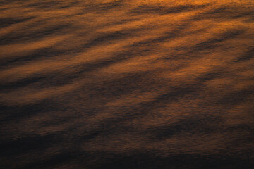 Abstract ocean water surface reflecting warm sunset light with gentle ripples, creating a calm and minimal natural texture suitable for background, luxury design, mindfulness, and atmospheric concepts