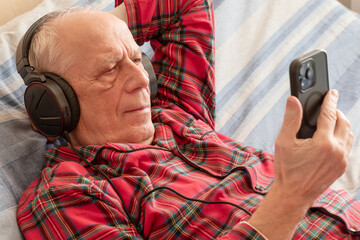 Happy Senior Man Using Smartphone and Headphones at Home. Modern Aesthetic Concept of Active Aging, Digital Literacy for Seniors, Video Calls, and Positive Lifestyle for Mature Generations