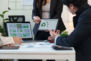 Business professionals collaborating on an ESG sustainability report and data analysis during an office meeting using a tablet and laptop to show environmental performance.