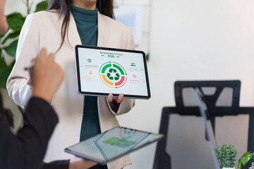 Woman in a white blazer holding a digital tablet presenting a Sustainable Future ESG infographic during a professional business meeting in a modern office.