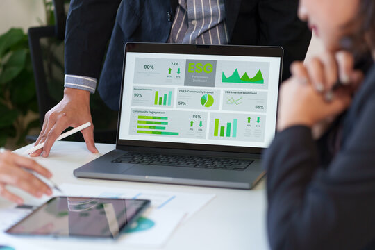 Business professionals analyzing an ESG performance dashboard on a laptop screen during a meeting to evaluate sustainability goals and corporate impact. - Powered by Adobe
