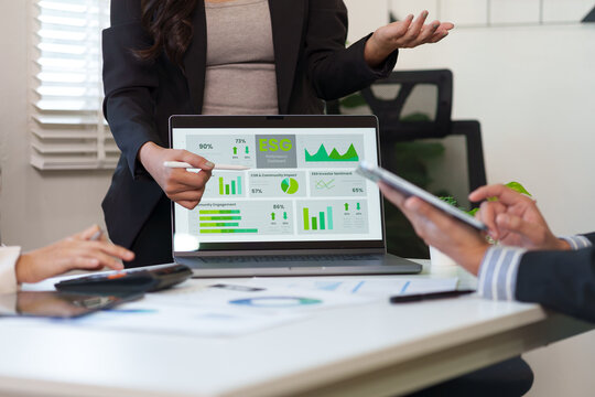 Business professionals analyzing an ESG performance dashboard on a laptop during a corporate meeting in a modern office. - Powered by Adobe