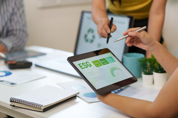 Business professional hands pointing at a tablet displaying ESG data and sustainability metrics during a corporate meeting in a modern office.