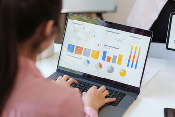 Female professional analyzing business data and financial charts on a laptop screen while working in a modern office environment.