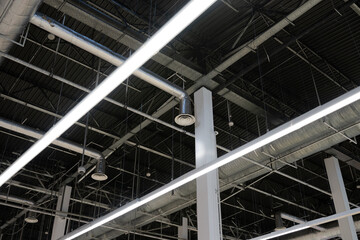 Industrial ceiling with exposed ventilation ducts, metal beams, and linear LED lighting inside a modern commercial or industrial building.