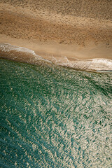 Top-down view of gentle ocean waves washing onto sandy beach with warm sunlight tones, creating a calm natural shoreline texture ideal for background, travel, wellness, and minimal design concepts.