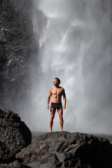 Fototapeta premium Daytime scene at Wallaman Falls with a fit man in swim trunks below the water fall, Queensland, Australia.