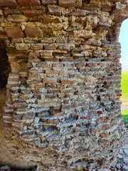Ancient weathered red brick wall with crumbling mortar texture, showcasing historic architecture and aged masonry detail.