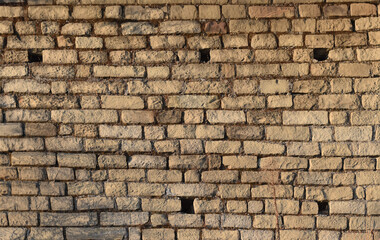 Fototapeta premium Old brick wall texture with uneven bricks and aged mortar. Vintage masonry wall made of weathered rectangular bricks. Historic brickwork surface showing timeworn construction details.