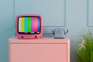 Pink retro TV set sits on a wooden desk in a modern home office apartment with a minimalist interior design featuring an old telephone. antique decoration style