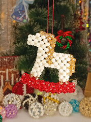 Handmade beaded horse ornament in white, gold and red colors, decorated as a festive Christmas and New Year decoration. Symbol of the Year of the Horse 2026. Hanging against the background of the tree