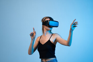 Woman wearing VR headset pointing at virtual interface, immersive digital interaction and futuristic technology concept on blue background