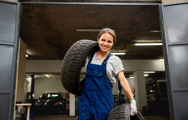Happy young female auto mechanic carrying tires in auto repair shop © Barillo_Images