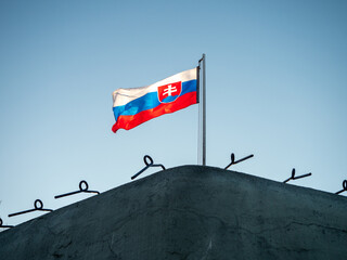Slovak national flag flying above a historic concrete military bunker in Petržalka, Bratislava, Slovakia, part of preserved prewar and Cold War fortifications.