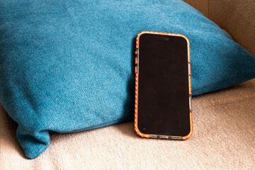 Smartphone with tortoise shell case leaning against teal blue cushion on beige sofa in living room