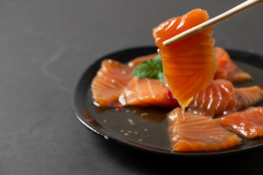 orean soy marinated salmon slices being picked with chopsticks, sauce dripping on black plate. Popular Korean food known as salmon jang, premium seafood