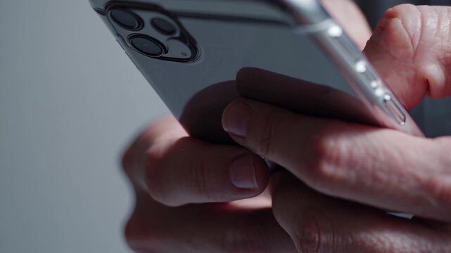 Man holding modern smartphone with silver casing. Scrolling on mobile device with hands for communication and browsing social media.