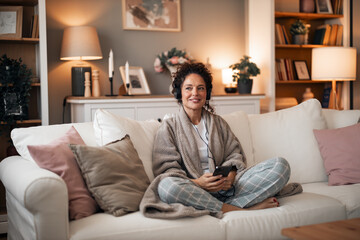 Obraz premium Cozy Home Moment: Woman Relaxed on Sofa With Headphones and Phone in Living Room