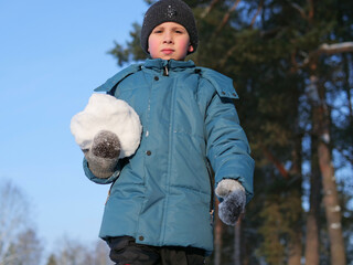 Close-up of a Child in a Blue Jacket Holding a Large Snowball watching down to camera - Winter Play: A Young Boy in a Beanie and Gloves Preparing for a Snowball Fight