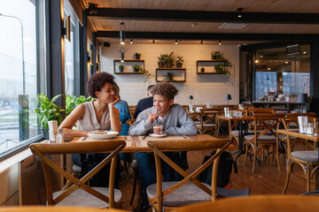 African American woman and her son are sitting in cafe drinking coffee and smiling, curly-haired teenager and his mother are having lunch in restaurant