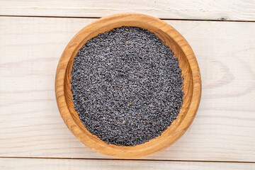 Dry poppy seeds with kitchen utensils on a wooden table, close-up, top view.