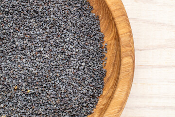 Dry poppy seeds with kitchen utensils on a wooden table, close-up, top view.