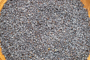 Dry poppy seeds in a wooden bowl, macro, top view.