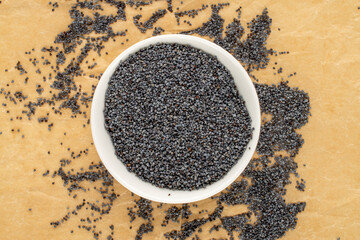 Dry poppy seeds with kitchen utensils on kraft paper, close-up, top view.