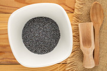 Dry poppy seeds with kitchen utensils on a wooden table, close-up, top view.