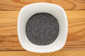 Dry poppy seeds with kitchen utensils on a wooden table, close-up, top view.