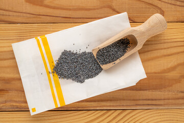 Dry poppy seeds with kitchen utensils on a wooden table, close-up, top view.