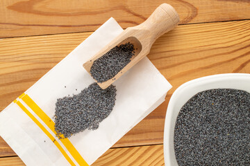 Dry poppy seeds with kitchen utensils on a wooden table, close-up, top view.
