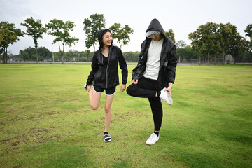 Two friends stretch their legs together on a green field, enjoying a light workout and friendly conversation outdoors
